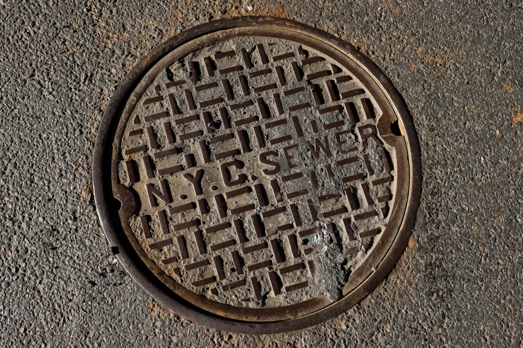 A circular metal manhole cover embedded in asphalt, inscribed with 