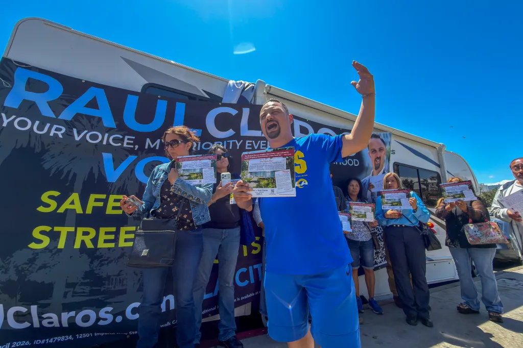 Raúl Claros with supporters at a news conference at MacArthur Park, holding up campaign fliers in front of an RV with a 