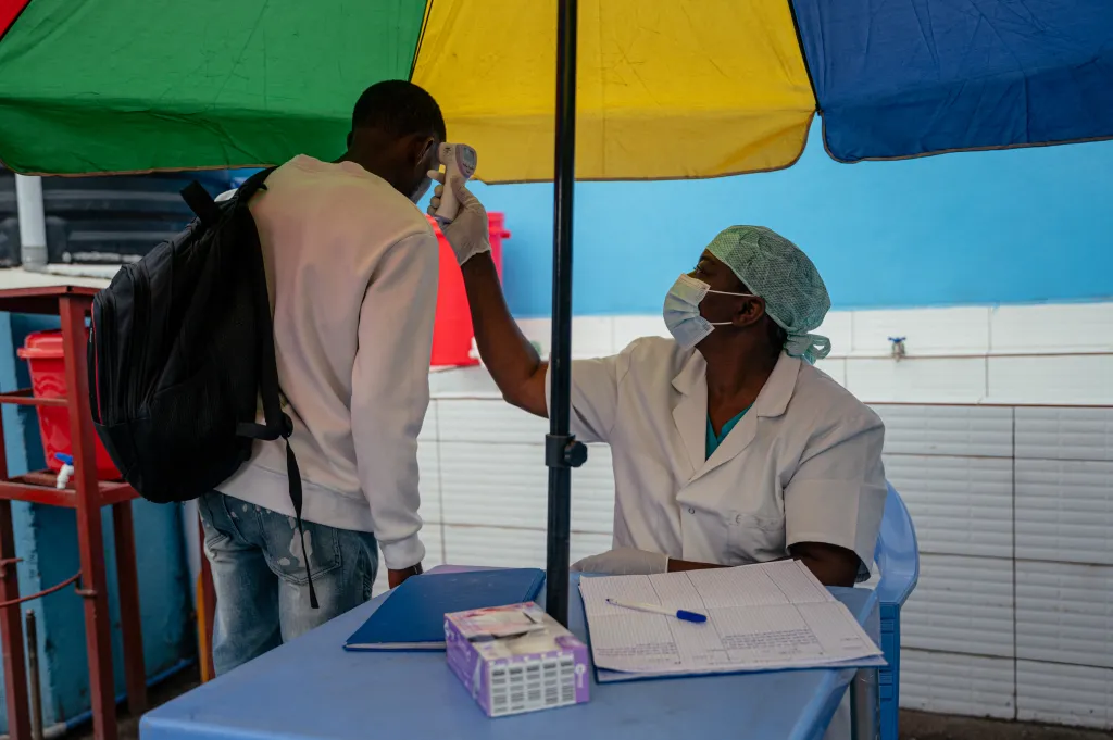 A health worker takes the temperature of a visitor at a hospital entrance.