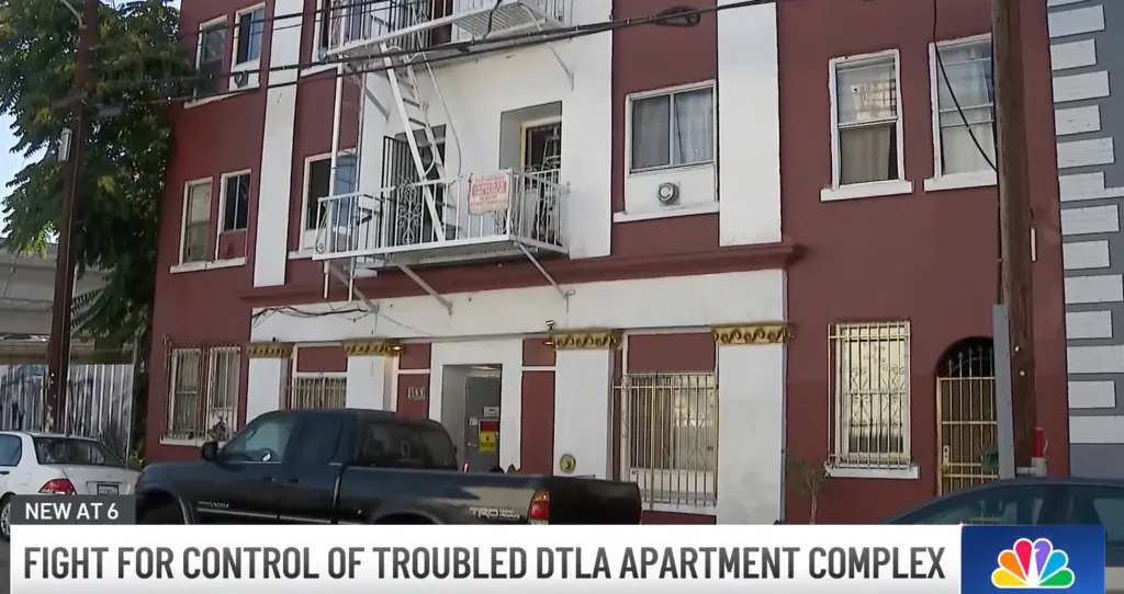 Exterior of an apartment building with red and white paint, visible fire escape, and barred windows.