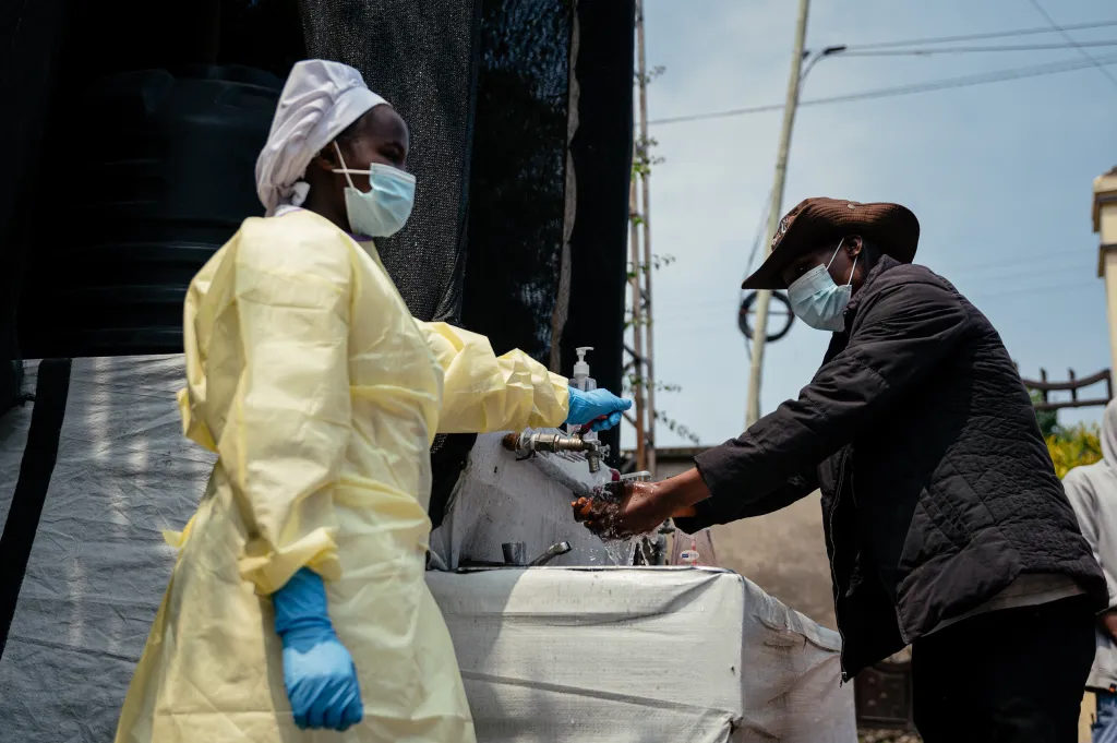 A person in protective gear helps a visitor wash their hands at an Ebola prevention checkpoint.