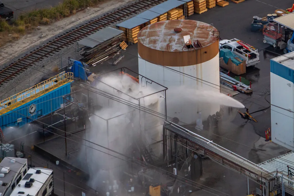 Aerial view of an overheated chemical tank being sprayed with water at an aerospace plant.