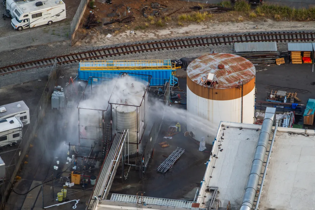 Aerial view of water being sprayed onto several overheated tanks at an aerospace plant.