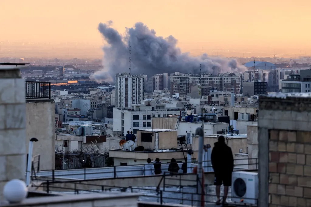 A plume of smoke rising from a strike in Tehran, with people observing from a rooftop in the foreground.
