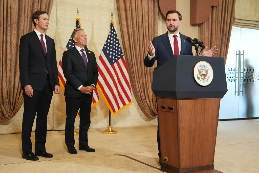 US Vice President JD Vance speaking at a news conference, with Jared Kushner and Steve Witkoff standing beside him.