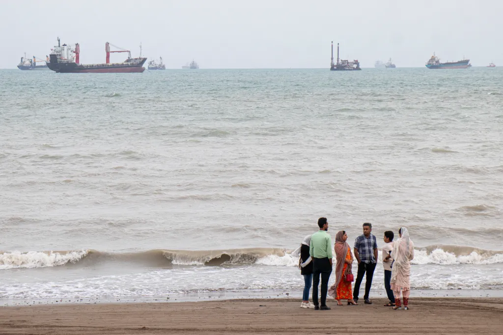 People on a beach in Bandar Abbas, Iran, with ships in the Strait of Hormuz.