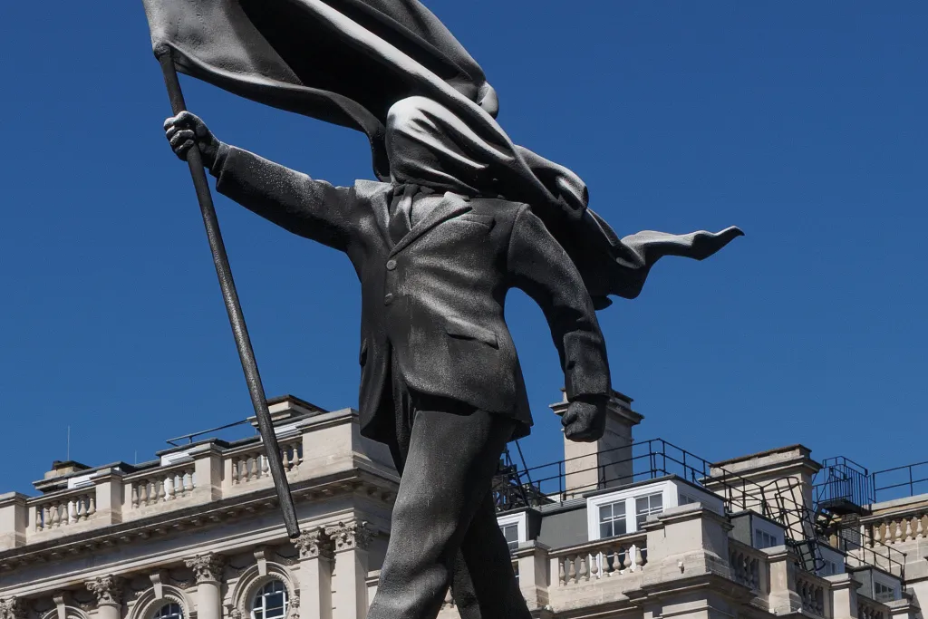Statue of a person in a suit, holding a flag that billows over their face.