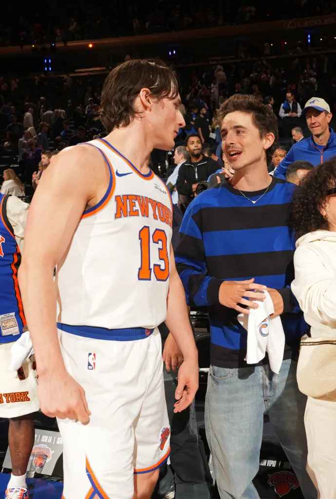 New York Knicks player Tyler Kolek and actor Timothee Chalamet speaking at a basketball game.