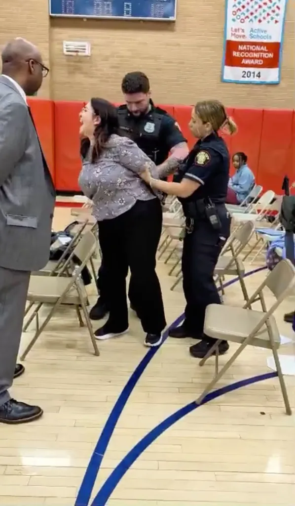 Two police officers arresting Emily Pecot at a school board meeting.