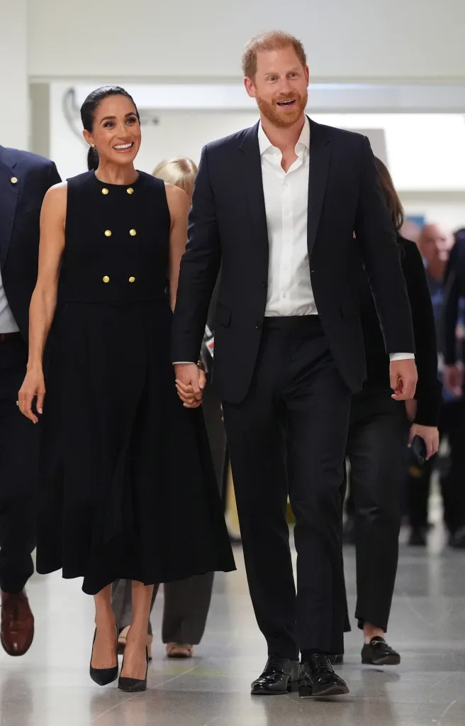 Meghan, Duchess of Sussex, and Prince Harry, Duke of Sussex, holding hands and smiling while walking.