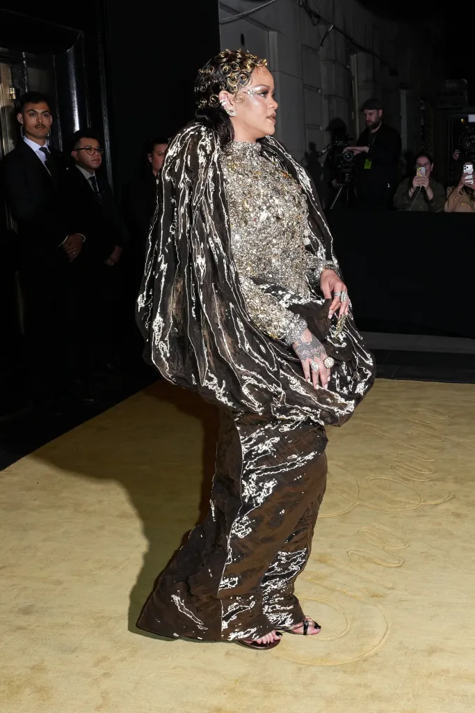 Rihanna in a black and gold sequined dress on a yellow carpet.