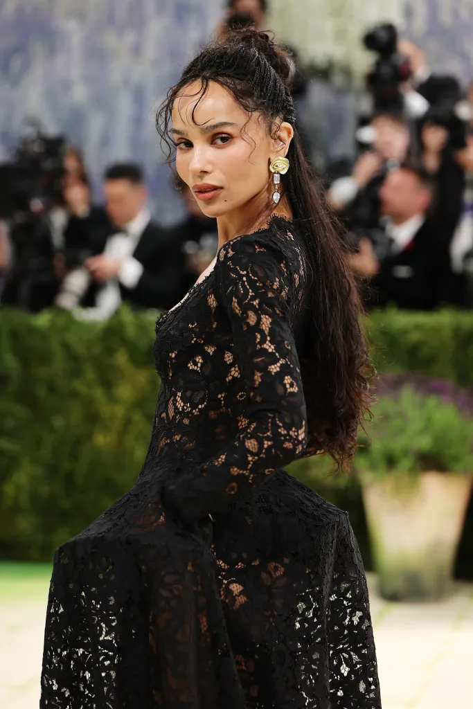 Zoë Kravitz in a long-sleeve black lace dress and gold floral earrings with hanging diamonds.