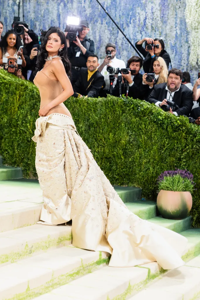 Kylie Jenner on the Met Gala red carpet, wearing a nude top and an ornate ivory skirt with a long train.