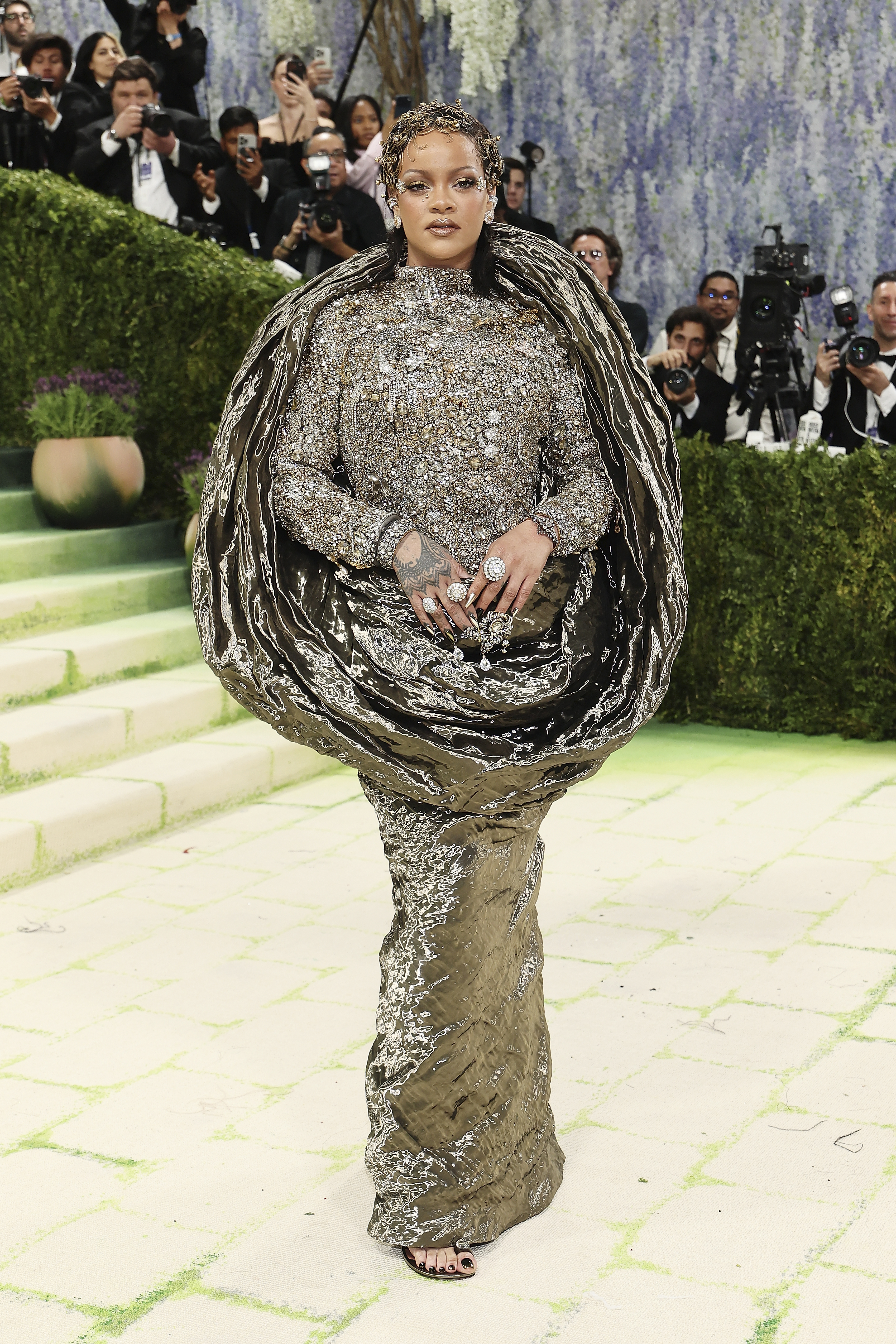 Rihanna attending the 2026 Met Gala wearing an embellished gold and silver gown with a sculptural, cape-like bodice.