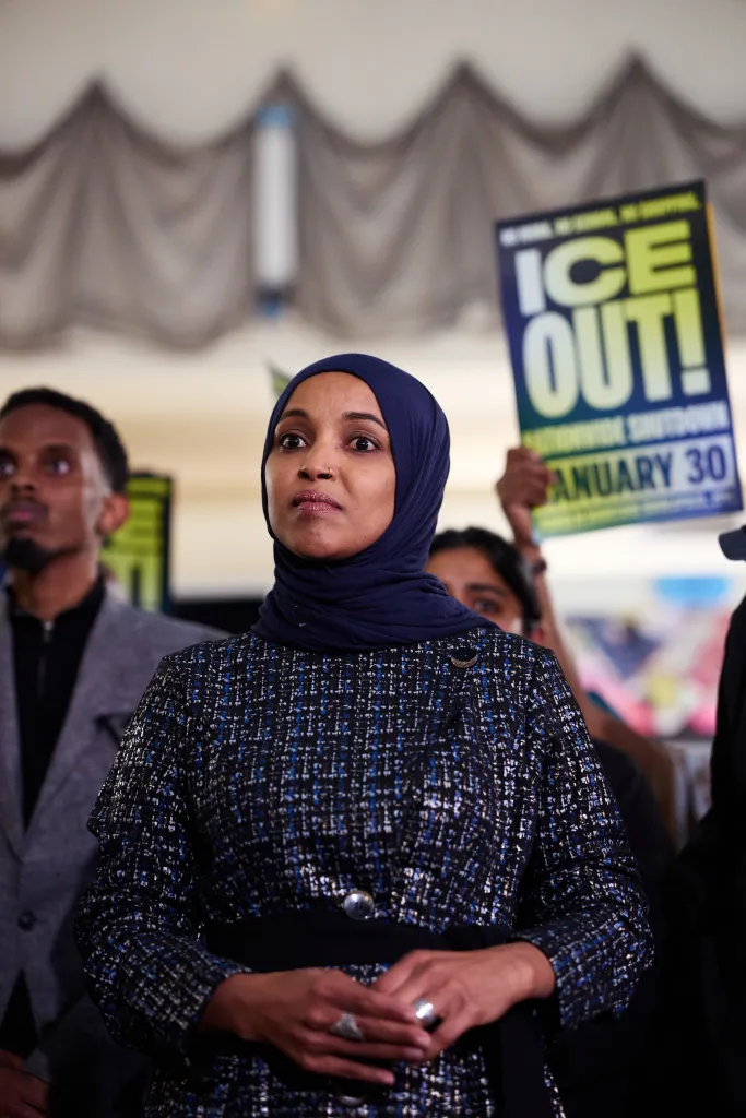 omar at a protest with a sign behind her reading ice out