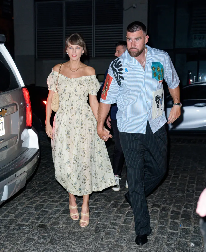 Taylor Swift and Travis Kelce hold hands while walking on a cobbled street.
