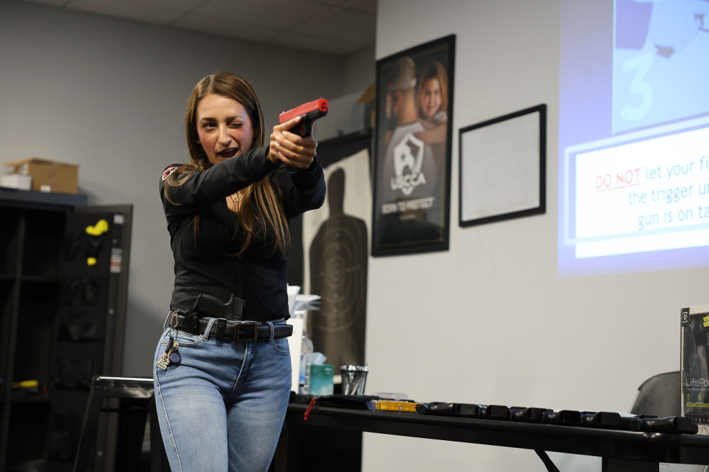 Georgia Worrell from the NY Post winks while aiming a red training pistol during a