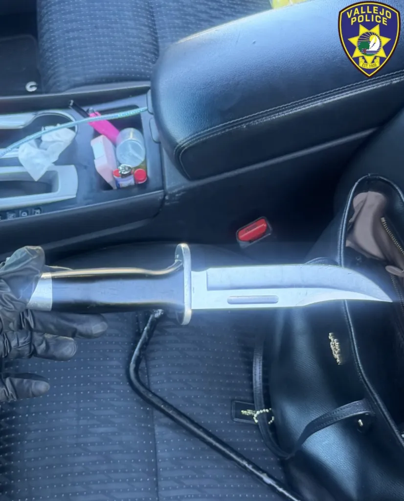 A gloved hand holding a large knife in a car interior, with a Vallejo Police logo in the upper right.