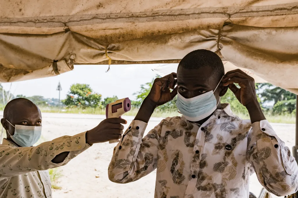 A border health officer checking a traveler's temperature with a contactless infrared thermometer at the Busunga crossing between Uganda and the Democratic Republic of Congo.