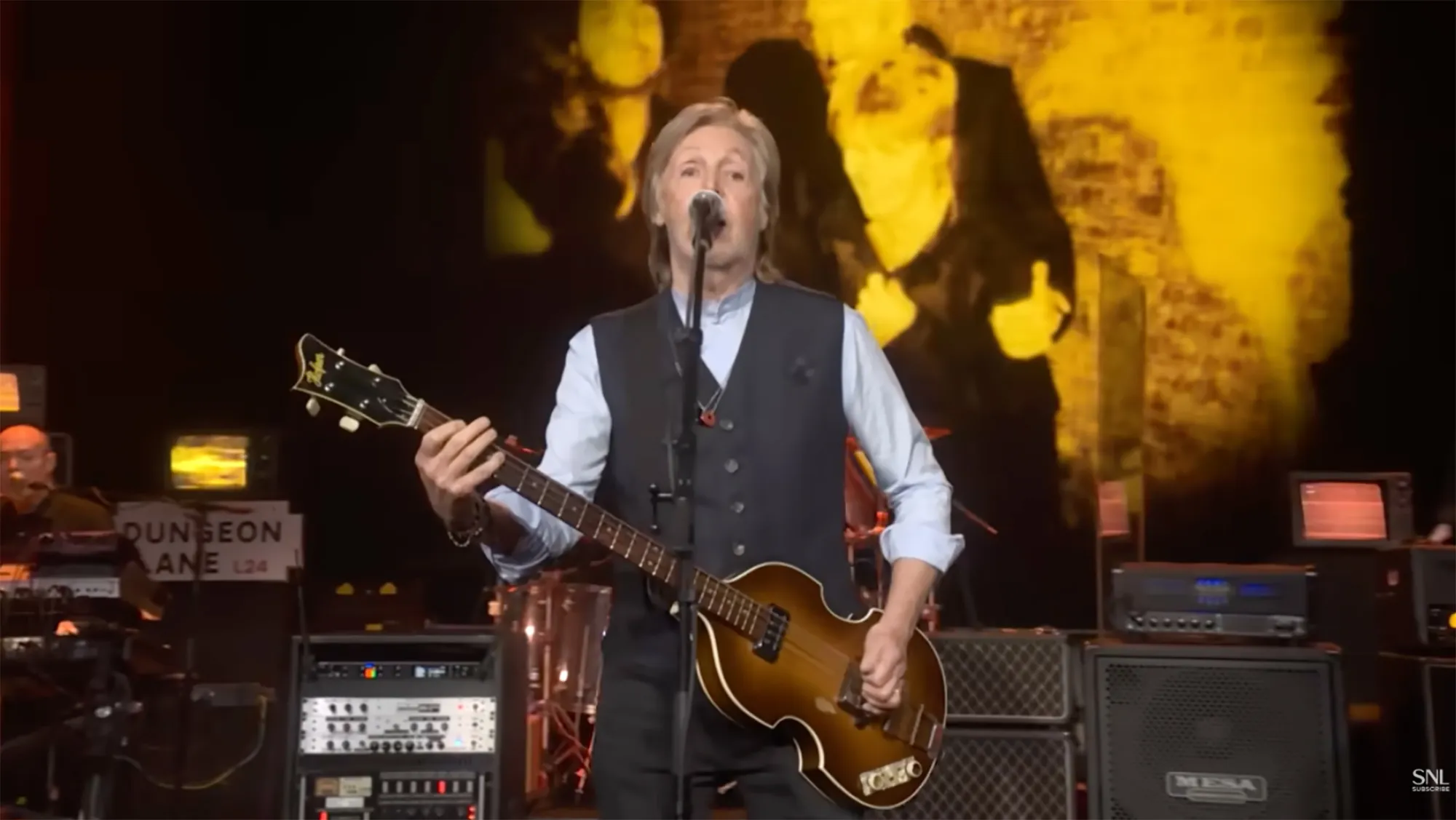 Paul McCartney performing live on stage while playing an electric guitar.