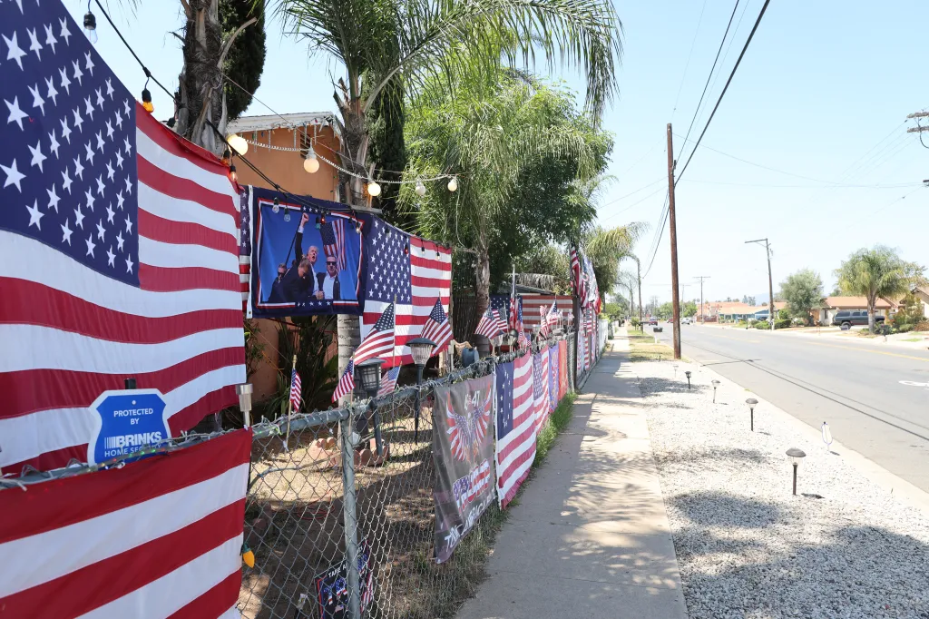 American flags and Trump banners displayed on a chain-link fence alongside a street.