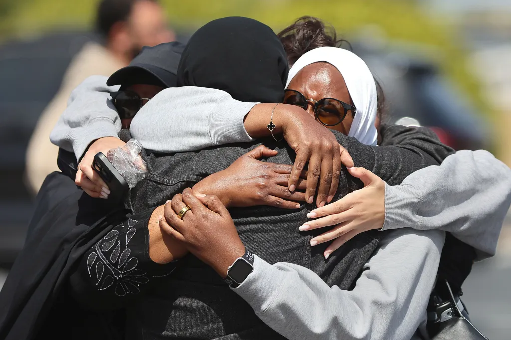 Three Muslim community members embrace following a shooting incident.