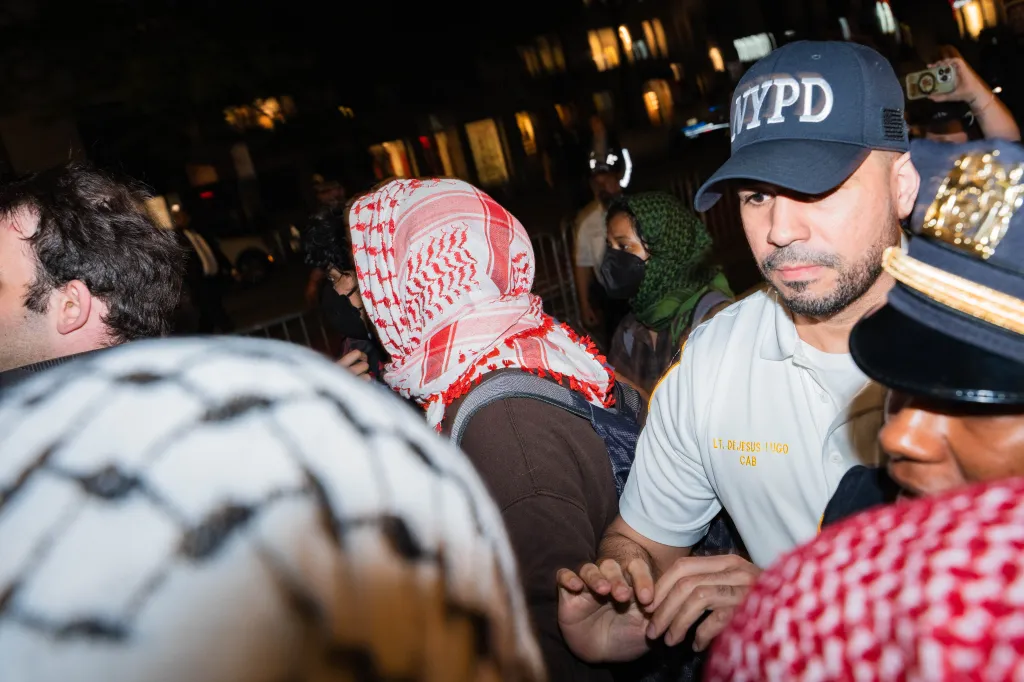 A man in an NYPD cap and shirt at an antizionist protest outside Park East Synagogue.
