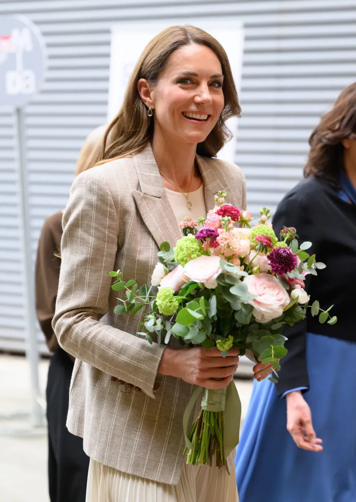 Catherine, Princess of Wales, smiles while holding a bouquet of flowers.