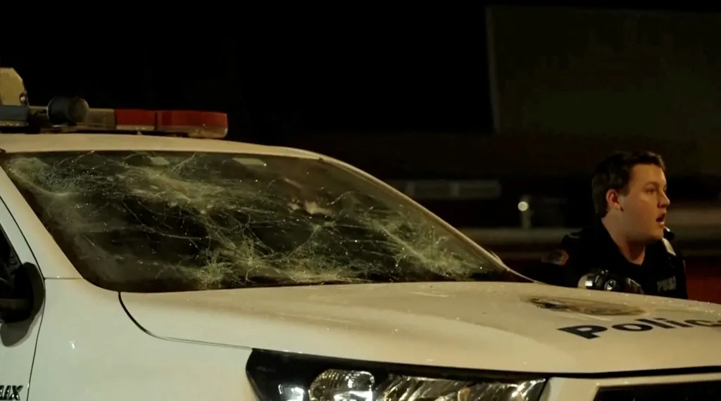 A police officer reacts next to a damaged vehicle during a riot outside of Alice Springs, Australia.