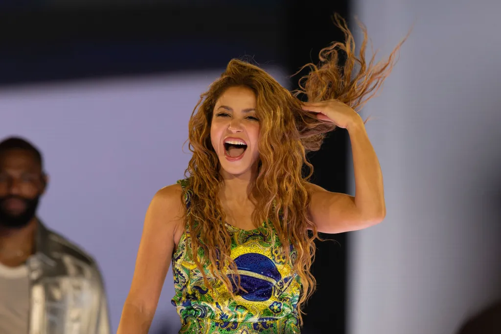 Shakira performing at a concert on Copacabana Beach, wearing a glittery green, yellow, and blue top.