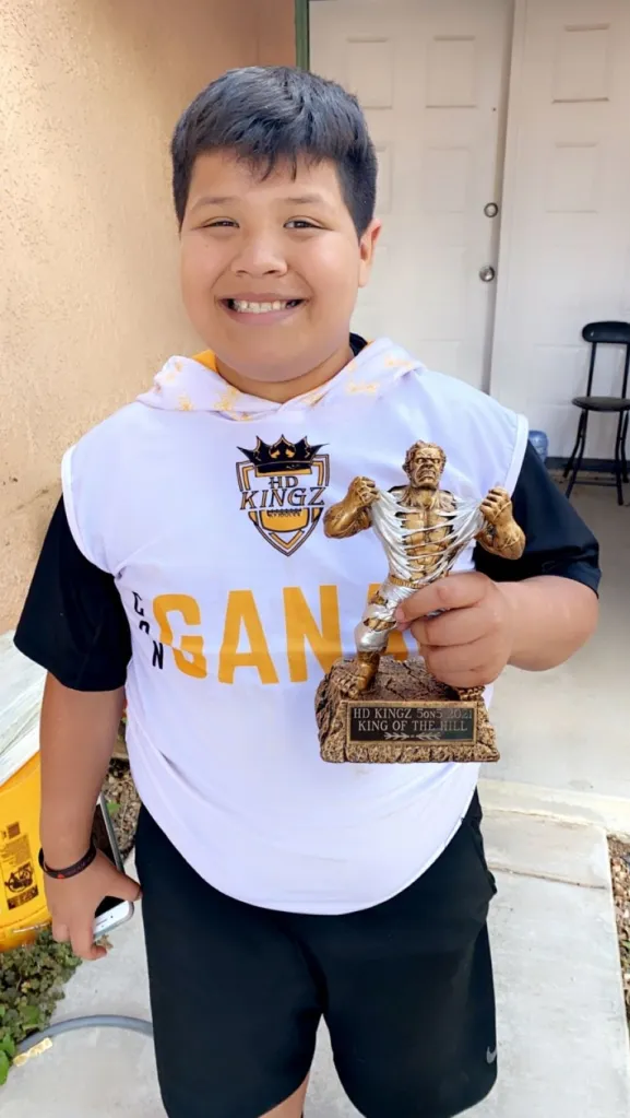 Jeremy Rosales, a boy with dark hair and a big smile, holding a trophy that says 