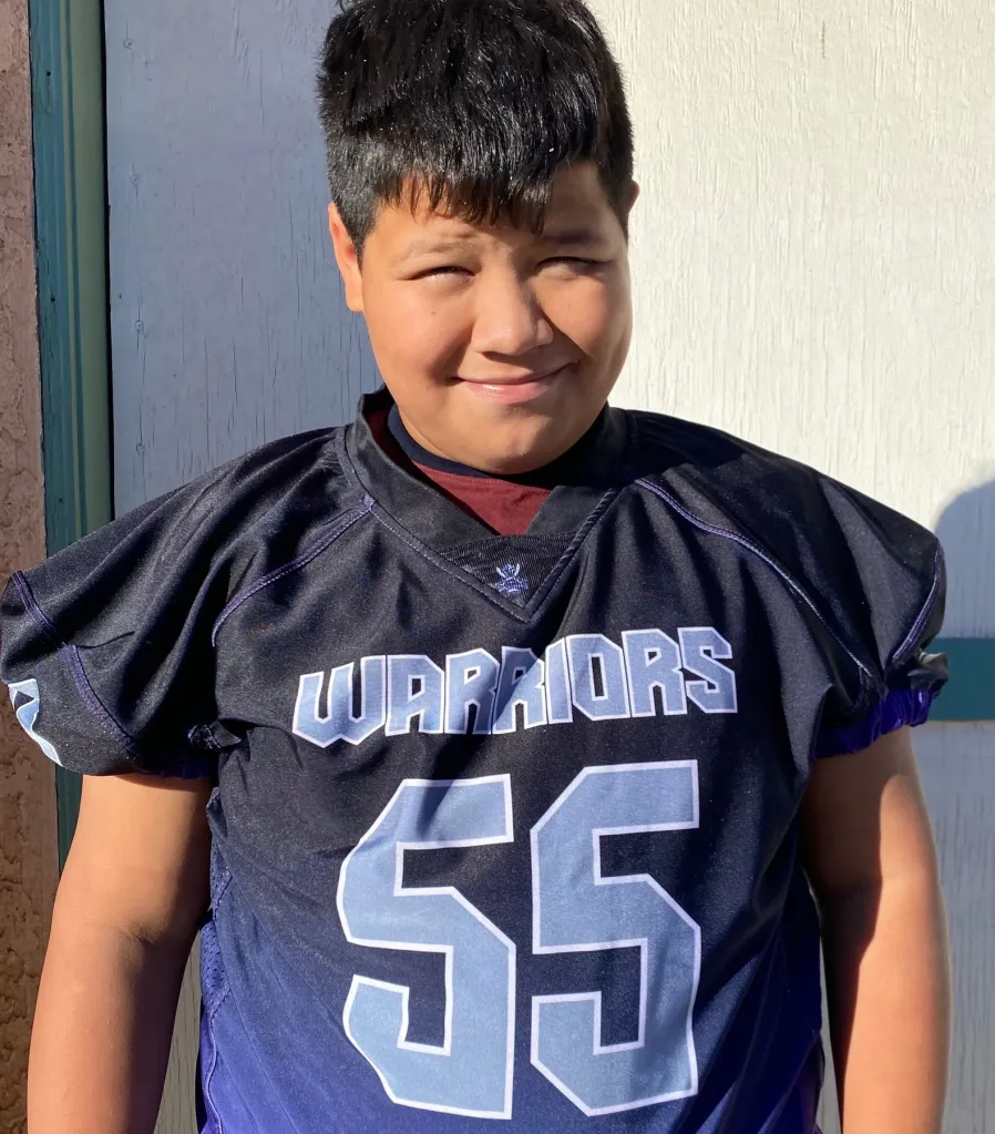 Jeremy Rosales, a young boy, smiles while wearing a black football jersey with 