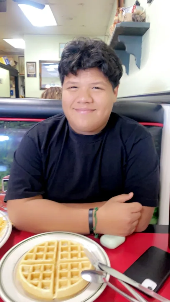Jeremy Rosales smiling in a restaurant booth with a waffle in front of him.