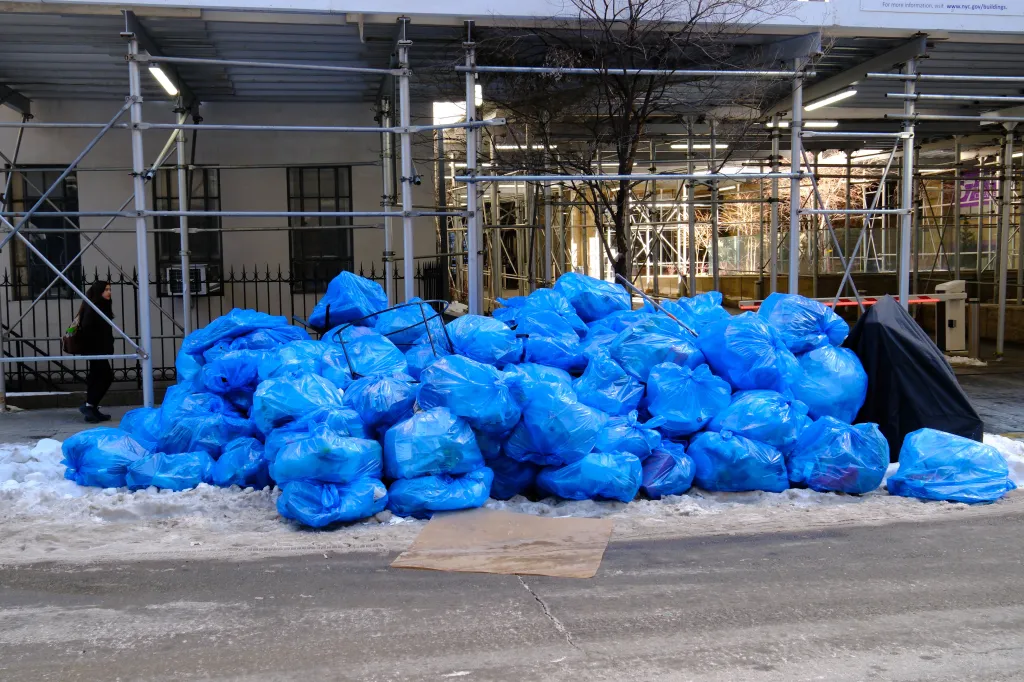 Piles of blue recycling bags on a snowy sidewalk in New York City.