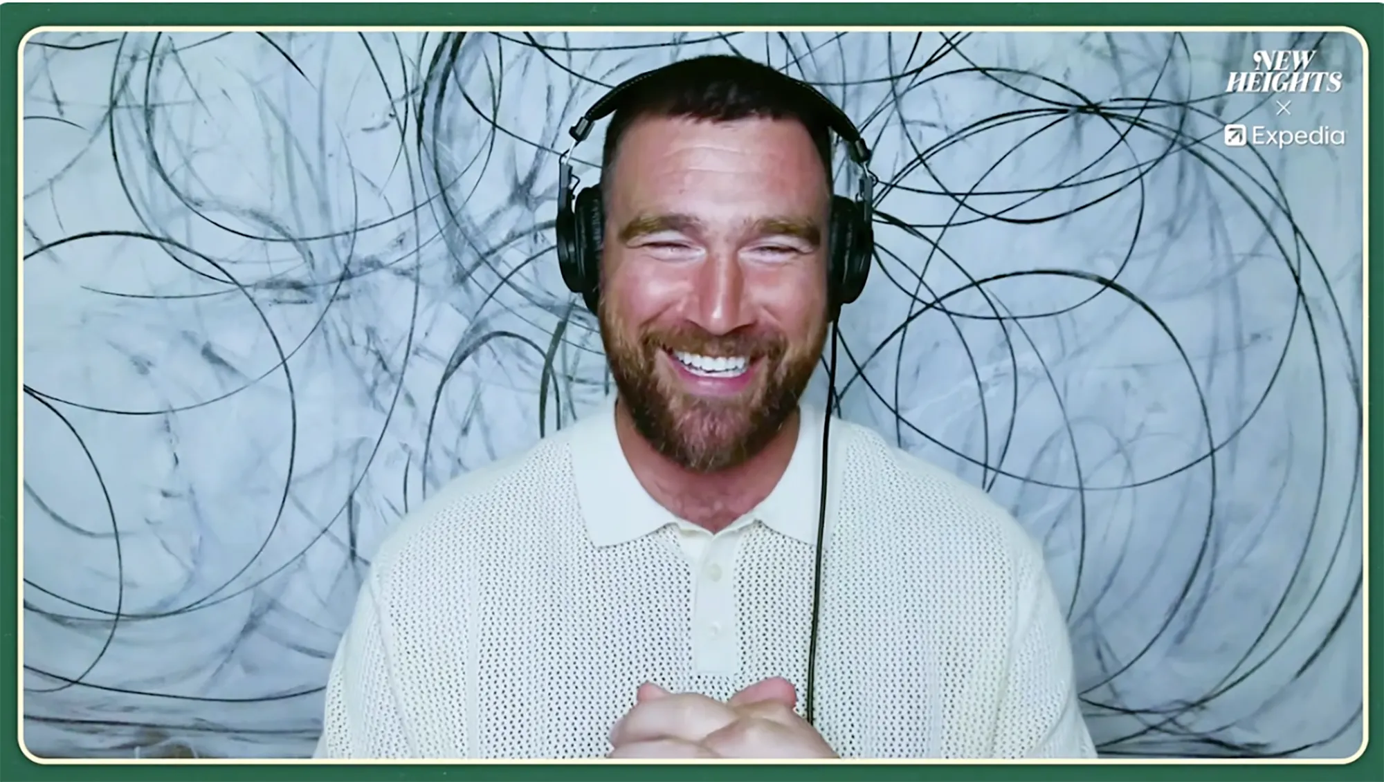 Travis Kelce laughing while wearing headphones and a white polo shirt, with a 
