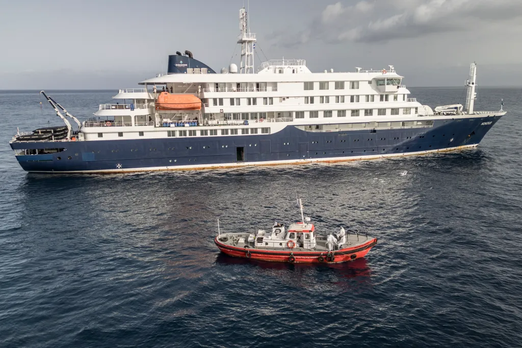 An aerial view of an ambulance boat with hazmat-suited crew approaching the cruise ship MV Hondius.