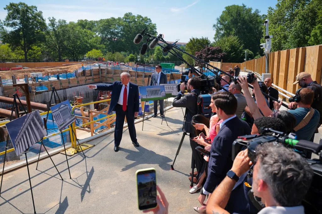 President Trump speaks to the media at the White House with proposed ballroom renderings and construction in the background.