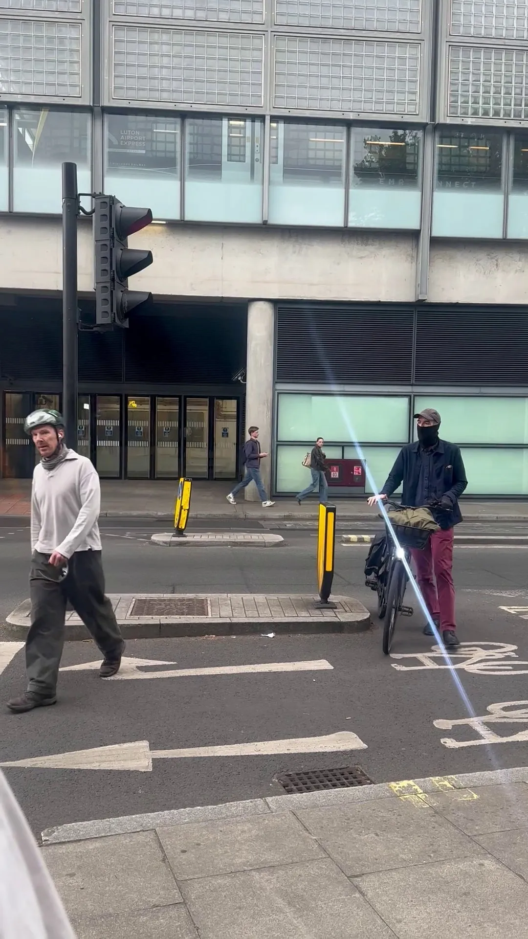 Benedict Cumberbatch in a cycling helmet and another cyclist in a mask stand on a street in London.