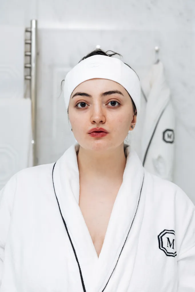 A woman in a white bathrobe with dark trim and a white headband.
