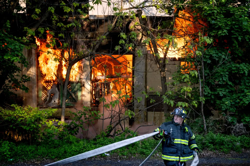 A firefighter directs a hose at a burning building engulfed in flames.