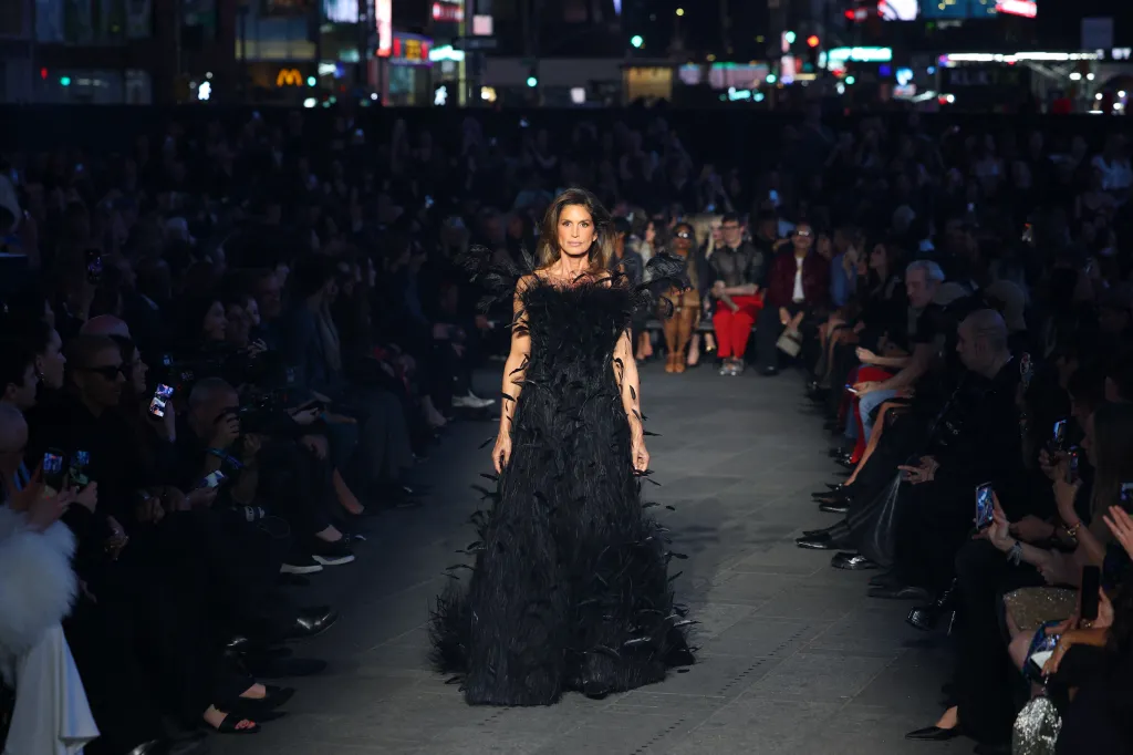 Cindy Crawford walks the runway in a long black feather dress during the Gucci Cruise 2027 fashion show.