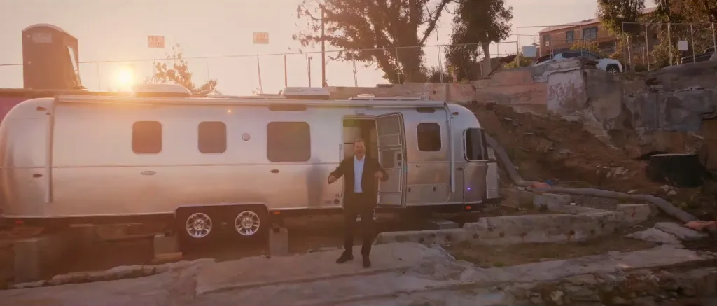 Spencer Pratt in a suit and open shirt standing in front of an Airstream trailer.