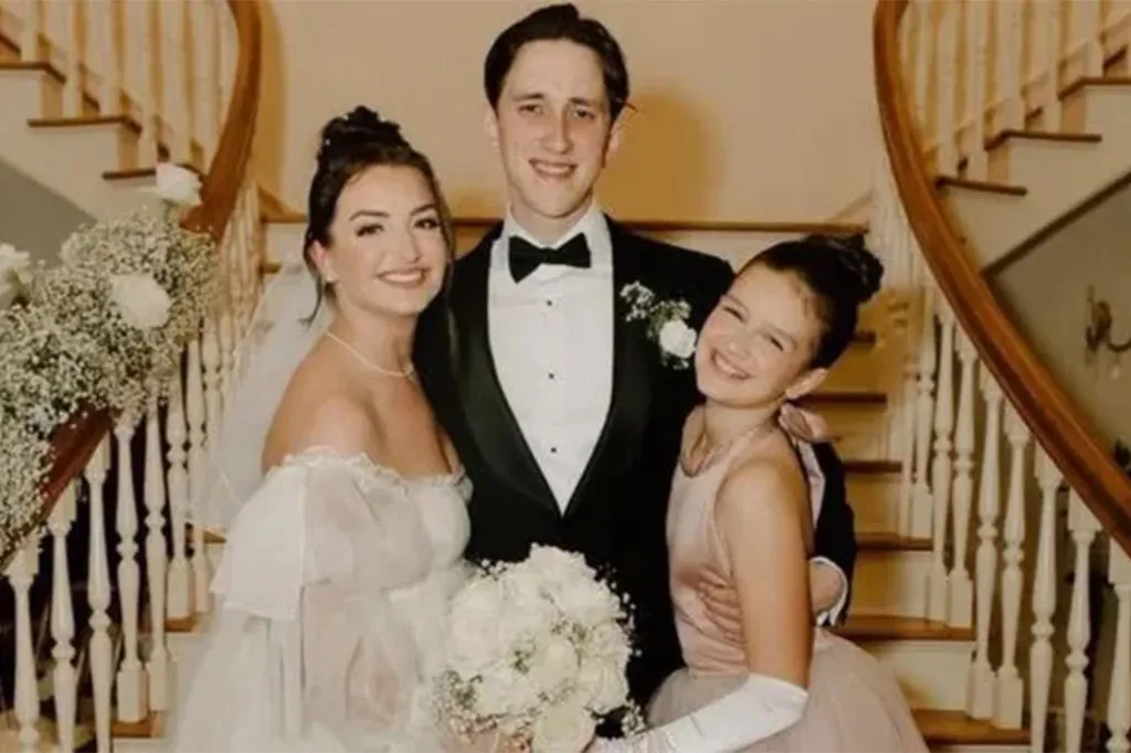 Jacob Nitkiewicz in a tuxedo standing between a woman in a wedding dress and a young girl in a pink dress, all smiling.