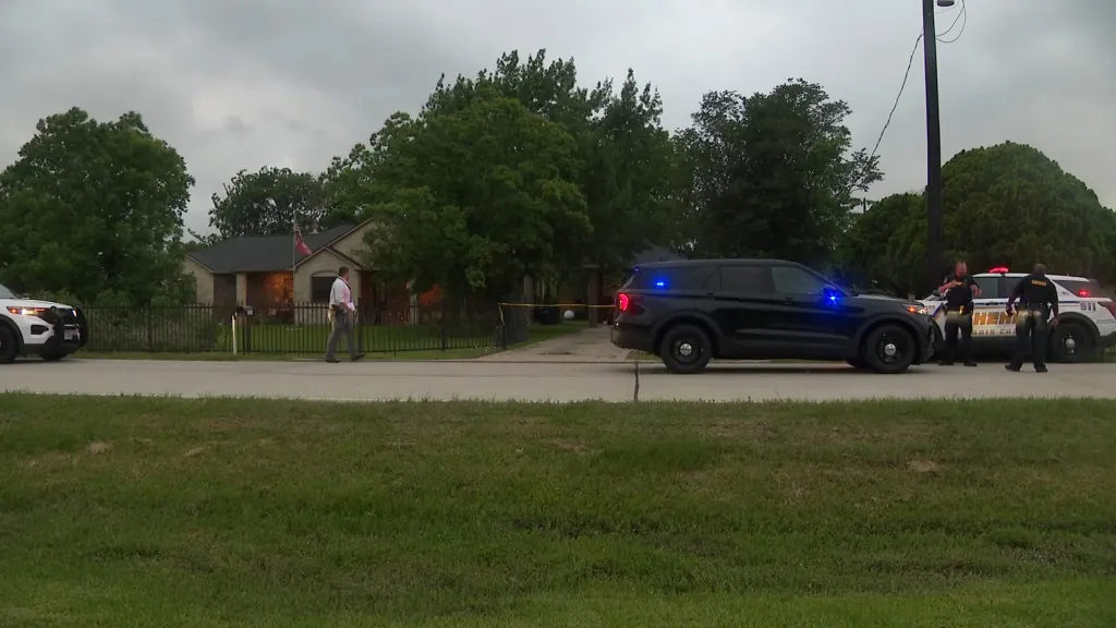 Police cars and officers on a street in front of a house, with a yellow tape across the driveway.