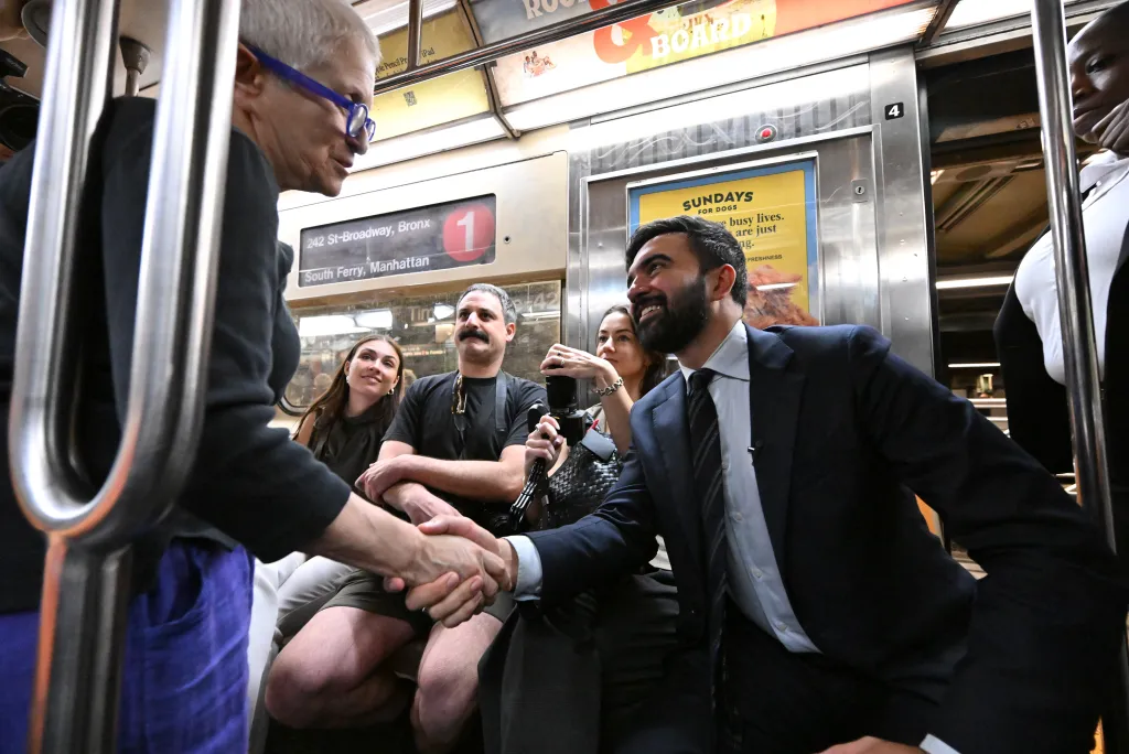 Zohran Mamdani shaking hands with a supporter on a subway train.
