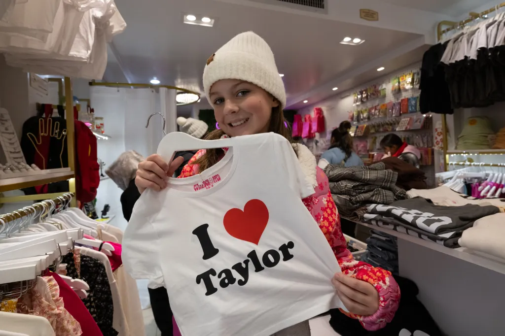 A young girl in a beanie holding up a white t-shirt that says 