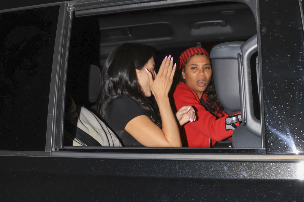 Kylie Jenner holding her hand to her face as Renell Medrano leans forward in a car.