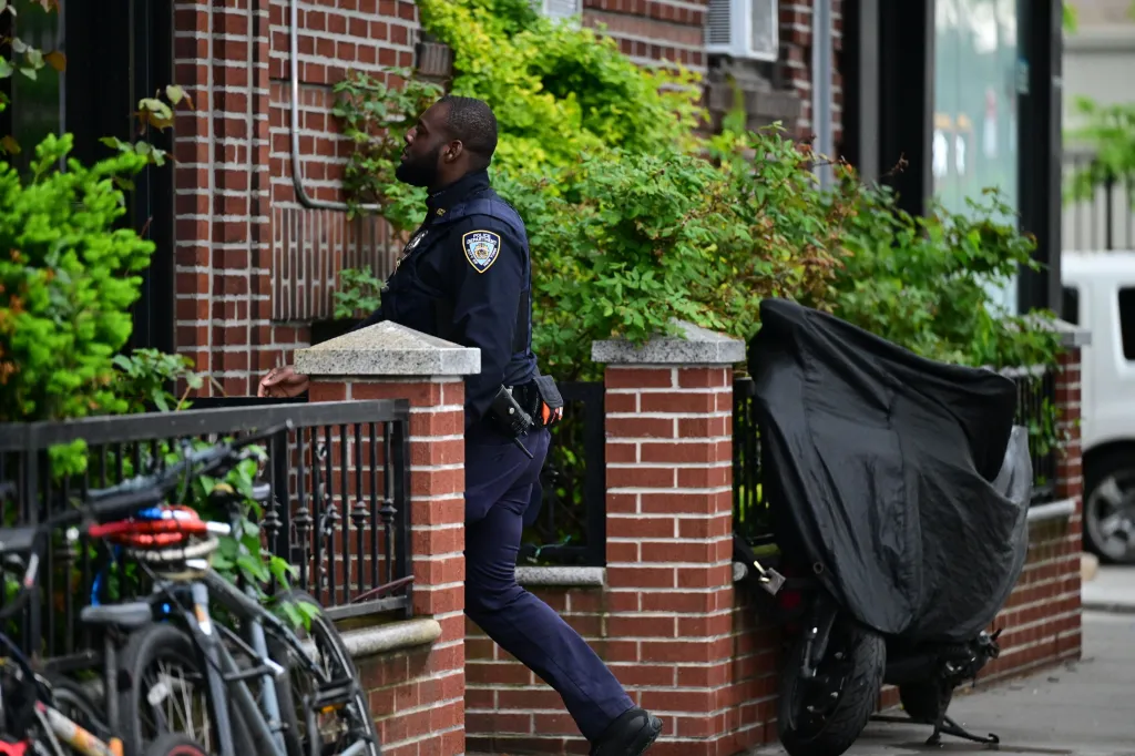 An NYPD officer investigates a crime scene outside a brick building in Brooklyn, New York.