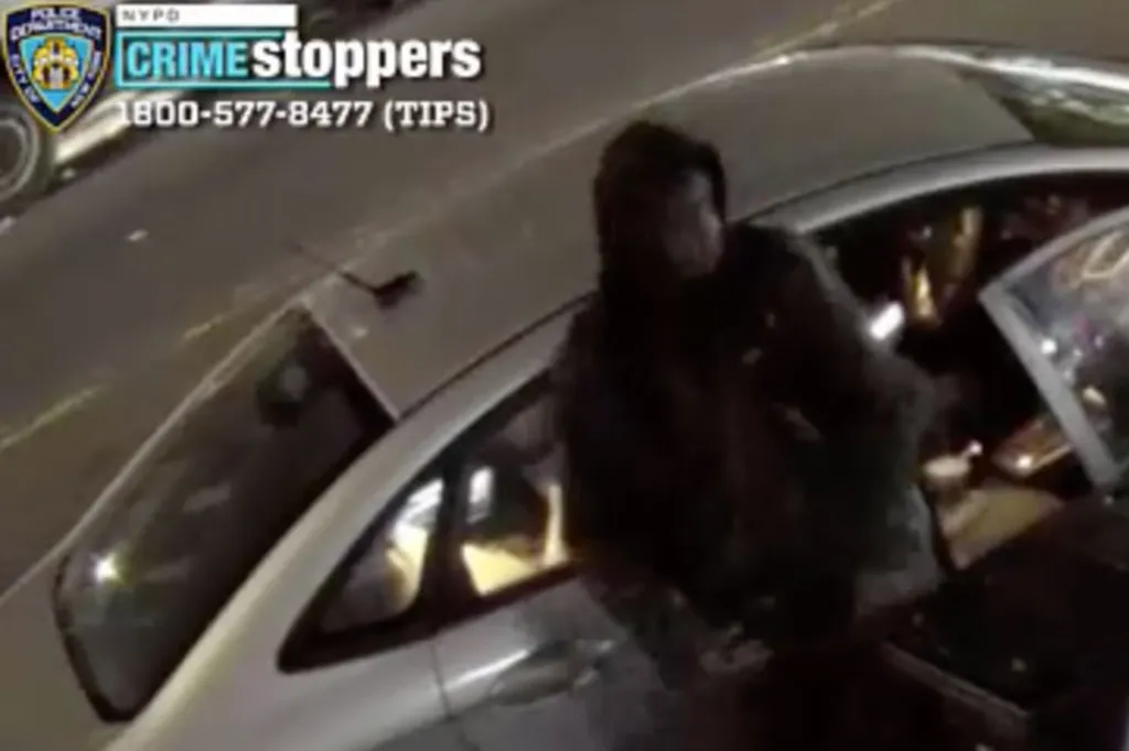 Still image from security footage showing a man with a dark complexion, wearing a dark hooded sweatshirt and black pants, getting into a silver car.