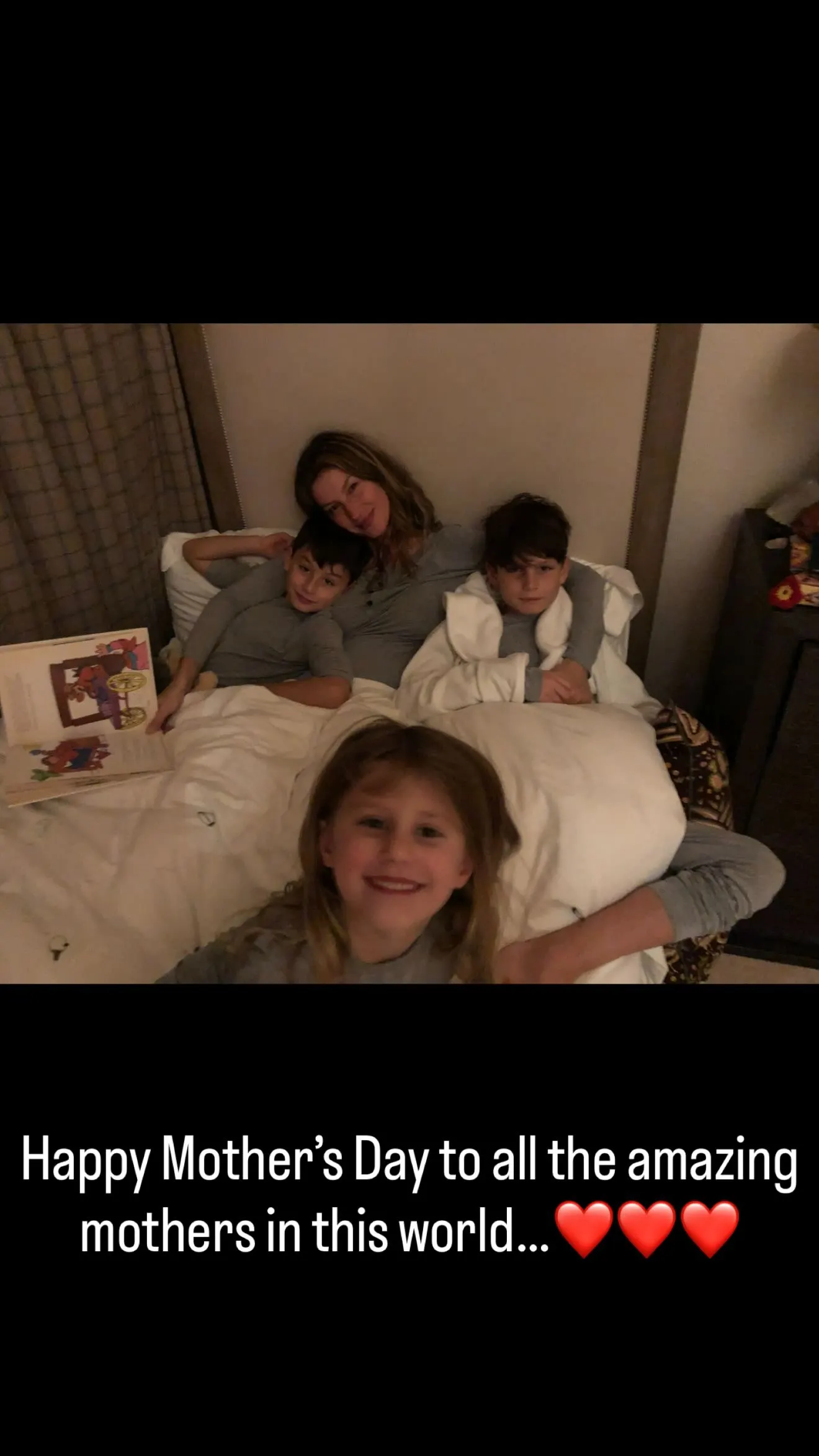 A mother and her three children lying in bed together, with text below wishing a Happy Mother's Day.